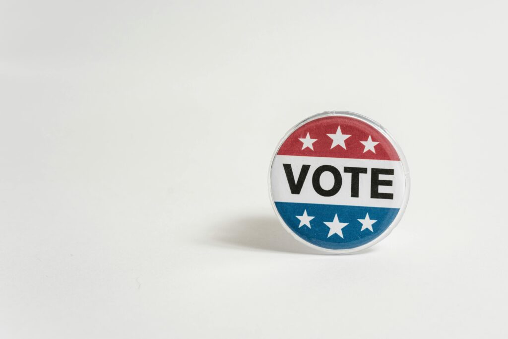 A circular pin with the word "vote" surrounded in red, white and blue.